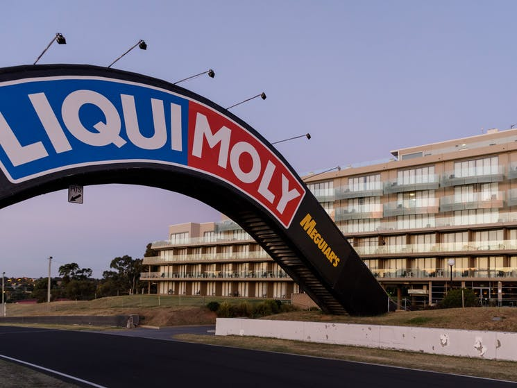 Rydges Mount Panorama hotel and its glazed balcony façade seen behind the circuit entry arch.